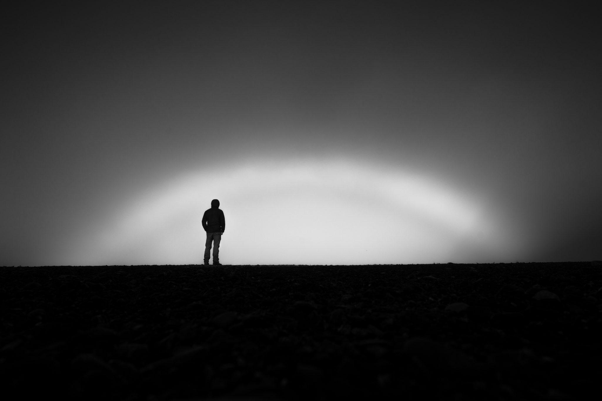 _DSC4991-Edit Black and white photo of man standing on a hill with sun coming up at dawn.