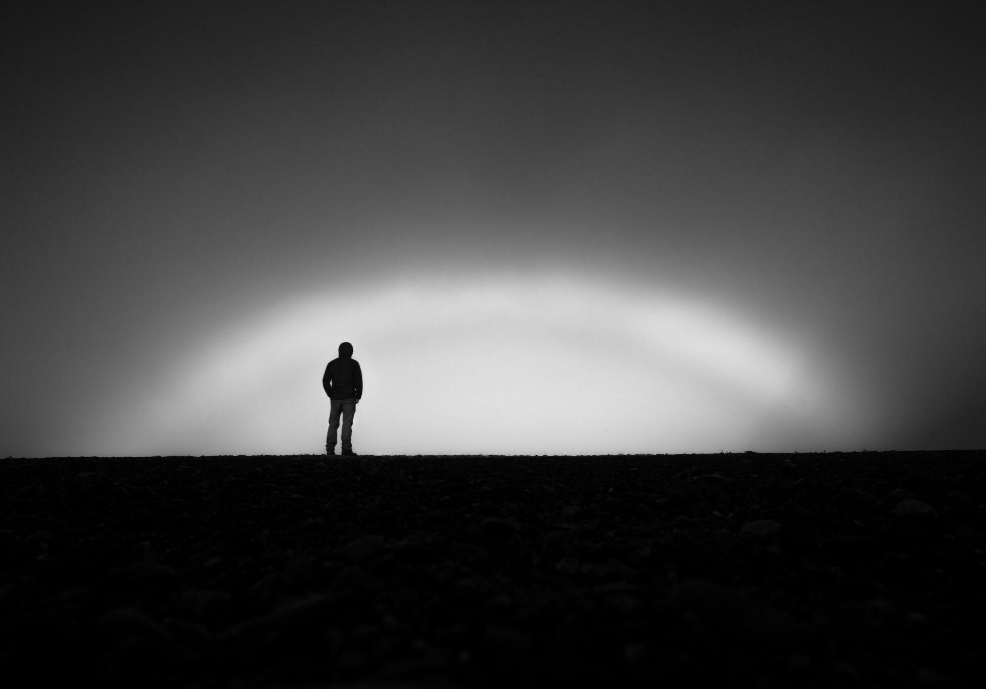 _DSC4991-Edit Black and white photo of man standing on a hill with sun coming up at dawn.